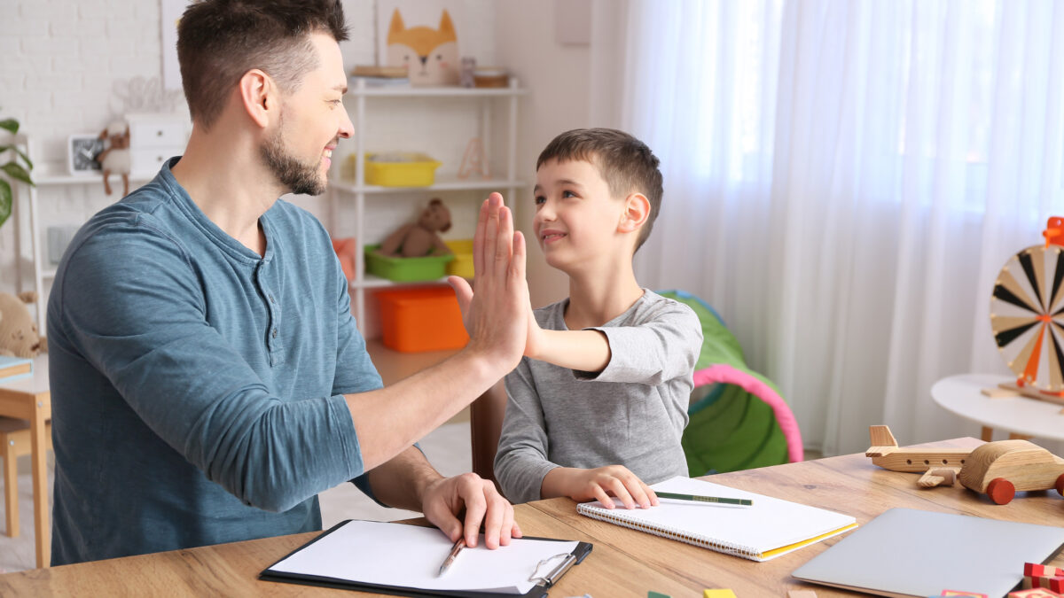 un enfant neuroatypique joue avec son papa sur le bureau main dans la main